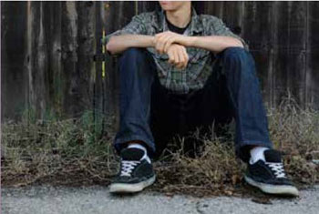 Teenager seated on the ground, with their face out of frame