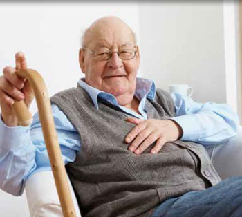 Male senior citizen, smiling, seated and holding a walking stick.